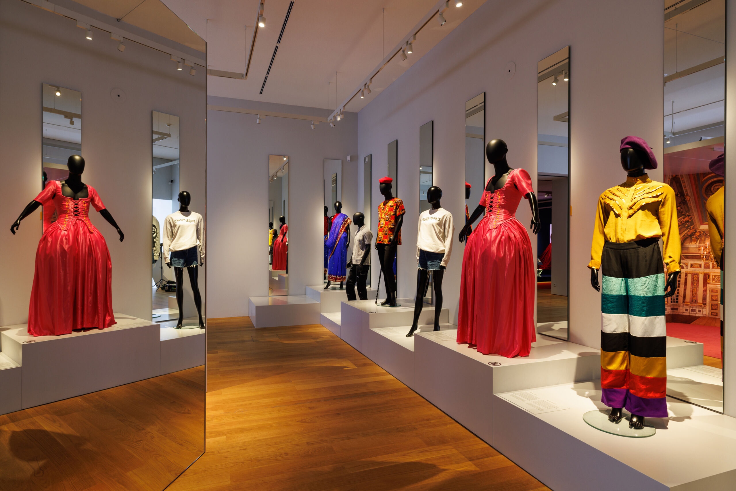 Tentoonstellingsruimte met geklede etalagepoppen op een wit podium.