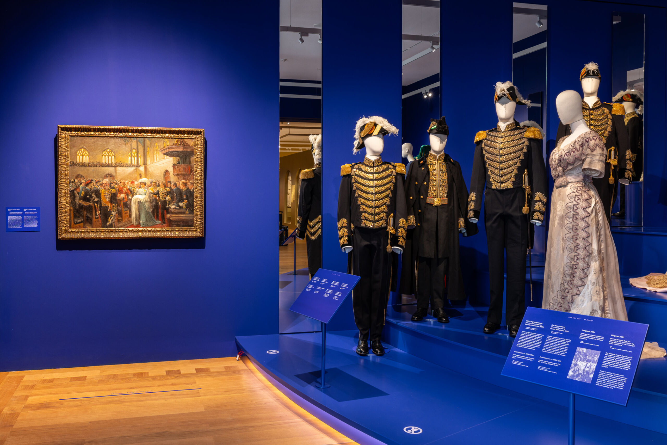 Tentoonstellingsruimte met geklede etalagepoppen op een blauw poium.