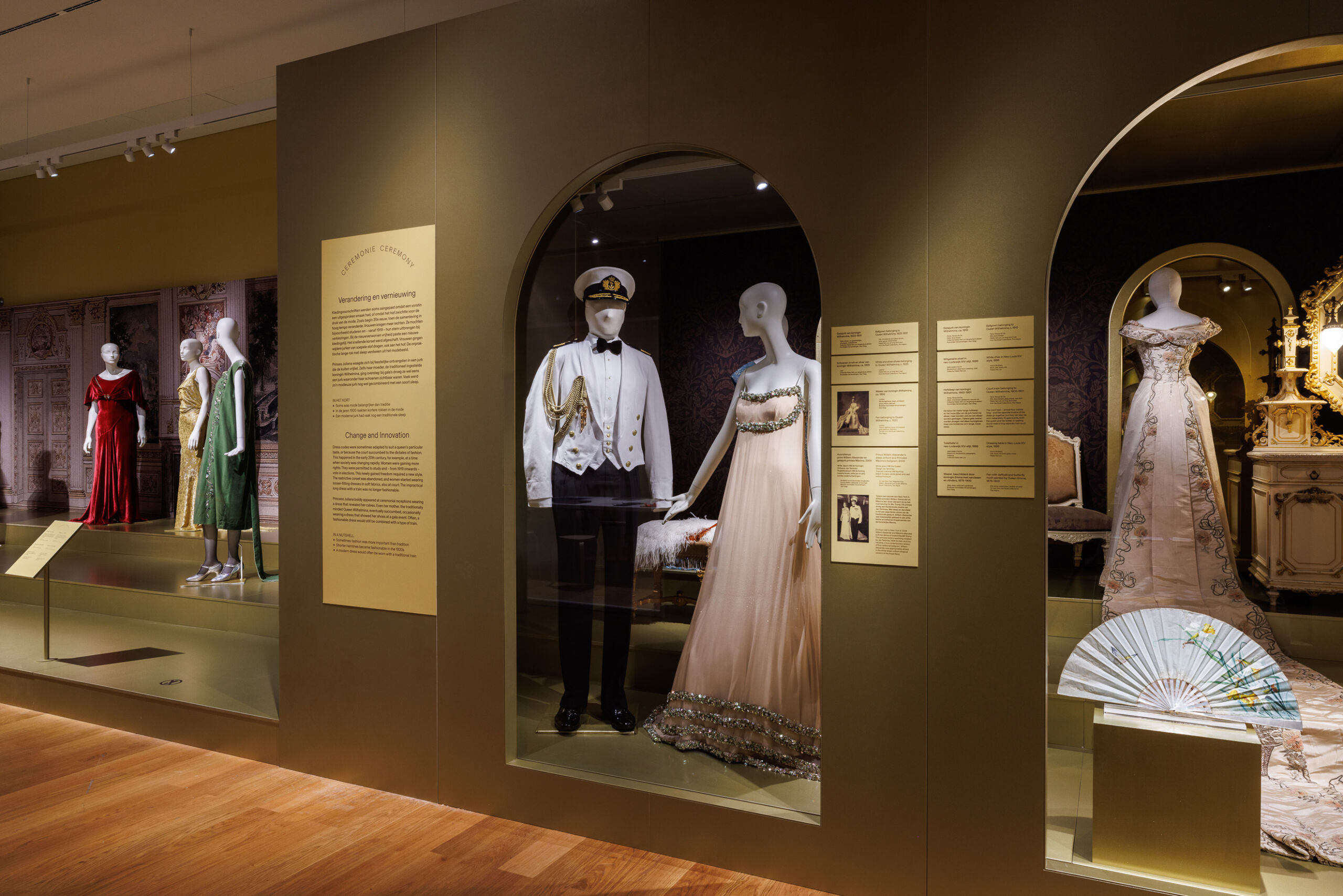 Tentoonstellingsruimte met geklede etalagepoppen in een groen podium.
